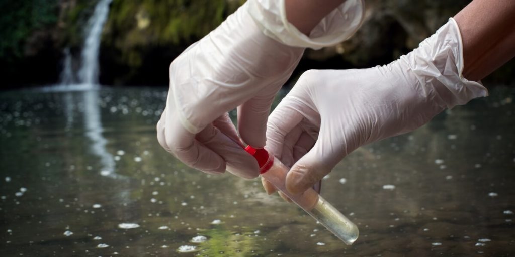 Gloved Hands Filling A Vial With Water